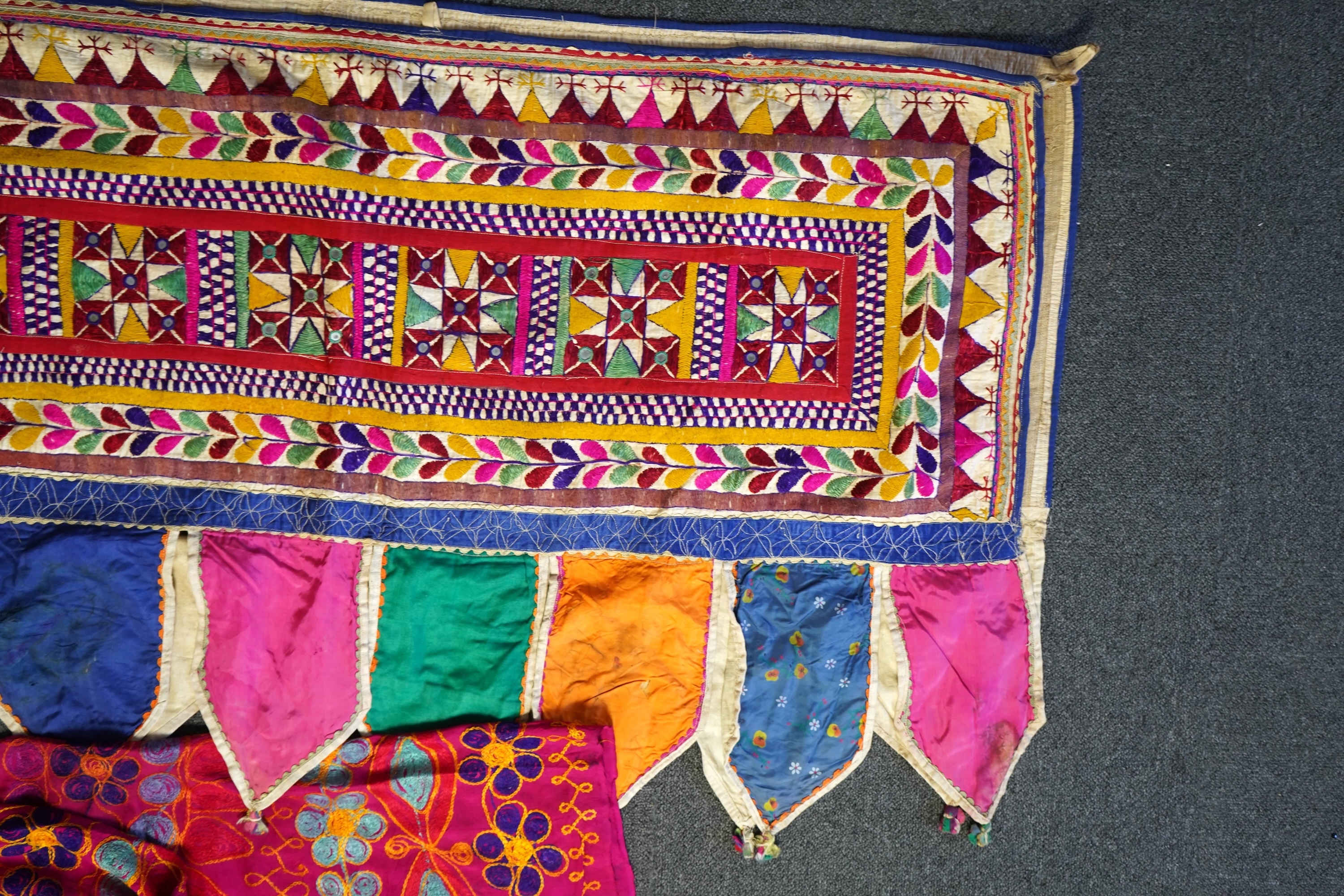 A large Indian silk embroidered and mirrored temple pelmet, with a cerise silk embroidered hanging and a length of cotton wax resist style printed fabric. Temple pelmet 468cm long x 70cm, deep. Condition - the pelmet has